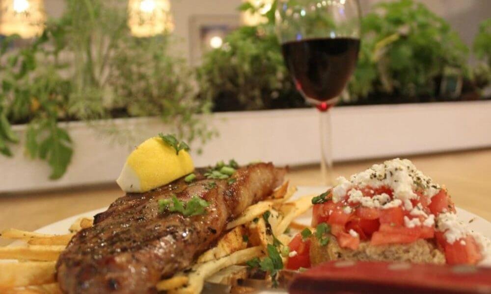 A plate of a steak on a bed of fries with a side salad and a glass of wine on the background